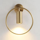 Gold ring and cylinder sconce lit against a plain pale wall