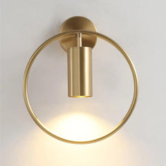 Gold ring and cylinder sconce lit against a plain pale wall