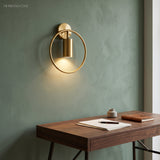 Brass ring sconce glowing on a green wall beside a wooden desk