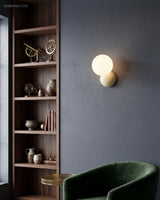 Wall sconce lit against a deep blue wall next to tall shelving and a velvet chair