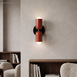 Terracotta cylinder sconce lit on a pale wall above a bookshelf
