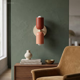 Red and terracotta sconce on a green wall above a wooden cabinet