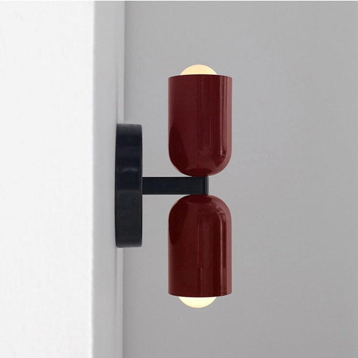 Two dark red cylinders lit on a grey wall beside a door frame