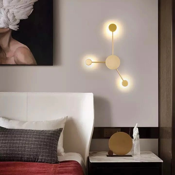 Gold three head wall sconce lit beside a bed with a red panelled wall