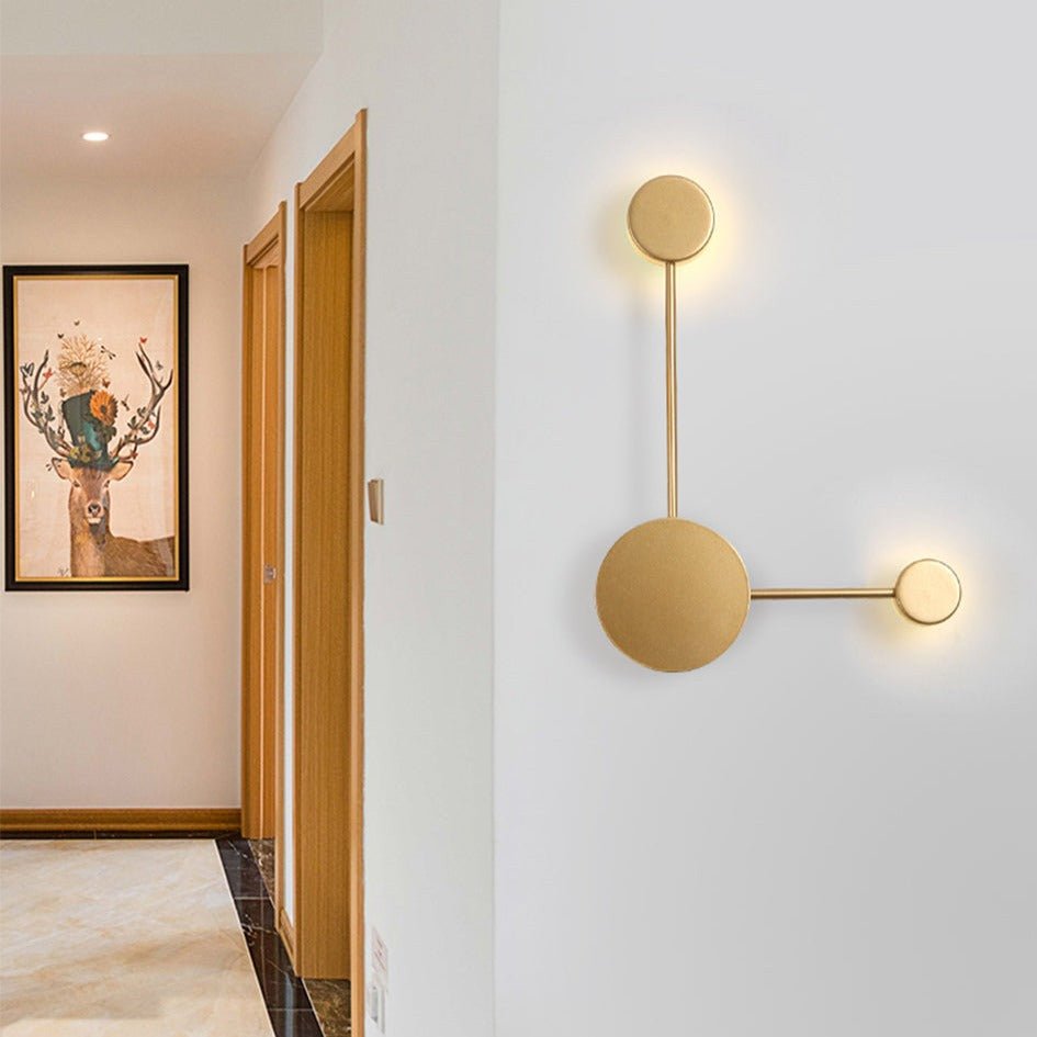 Gold three head wall sconce lit in a hallway beside a framed print