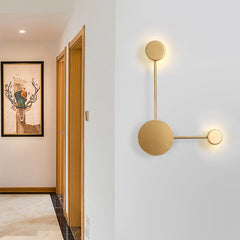 Gold three head wall sconce lit in a hallway beside a framed print