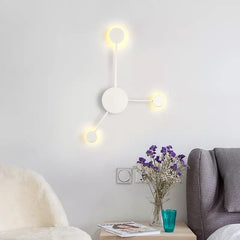 White three head wall sconce lit above a side table in a living room