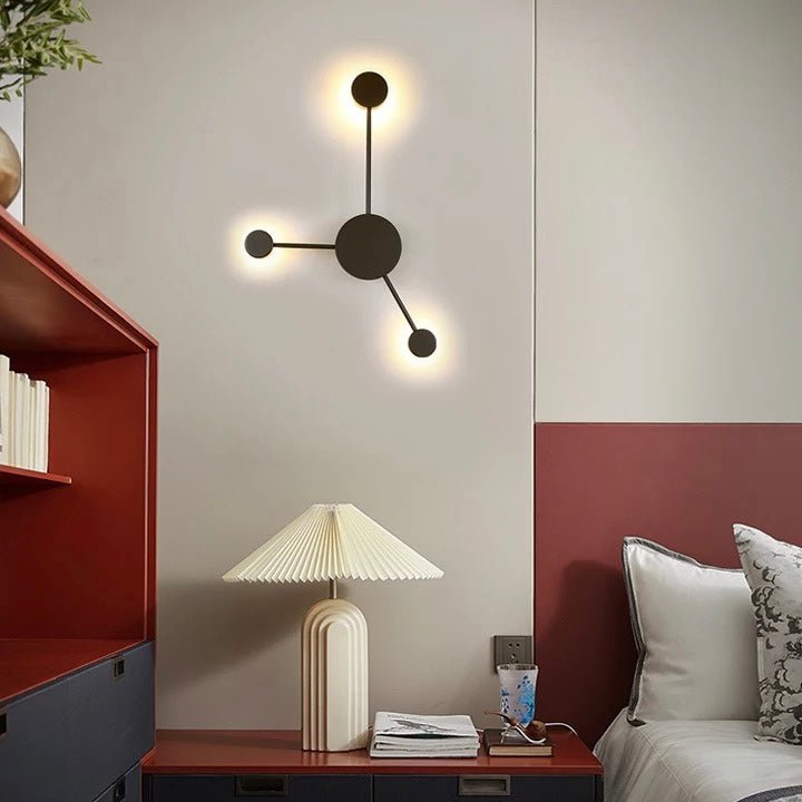 Black three head wall sconce lit above a sideboard with a table lamp