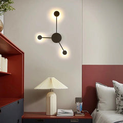 Black three head wall sconce lit above a sideboard with a table lamp