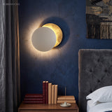 White and gold disc sconce casting a halo behind a bedhead