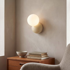 Modern wall sconce with an opal globe offset above a cream round backplate