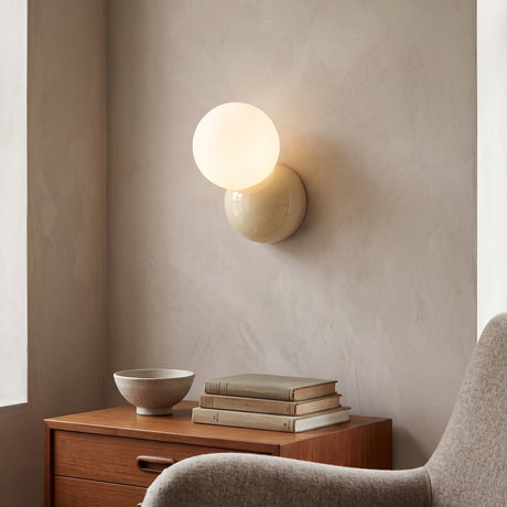 Modern wall sconce with an opal globe offset above a cream round backplate