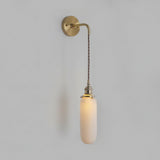 Slim capsule shade lit warm on a cord against a grey wall