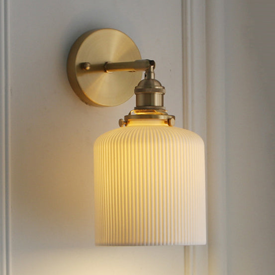 Ribbed drum shade lit warm on a brass arm against white panelling