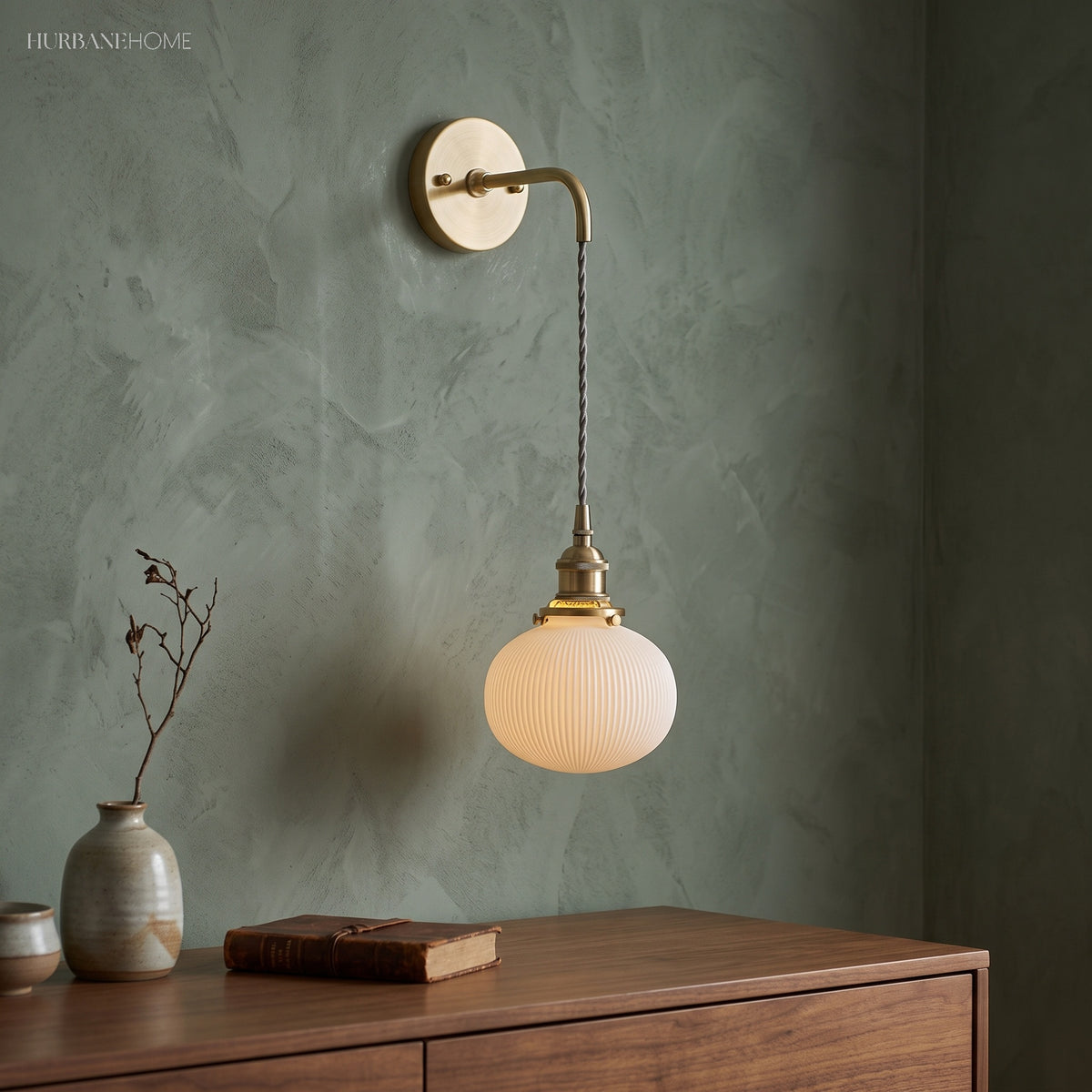 Small white shade on a braided cord against a mottled green wall