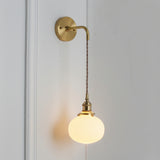 Small round white shade glowing warm on a braided brass cord