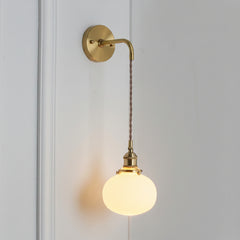 Small round white shade glowing warm on a braided brass cord