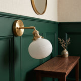 Brass sconce with a ribbed white shade on a deep green wall