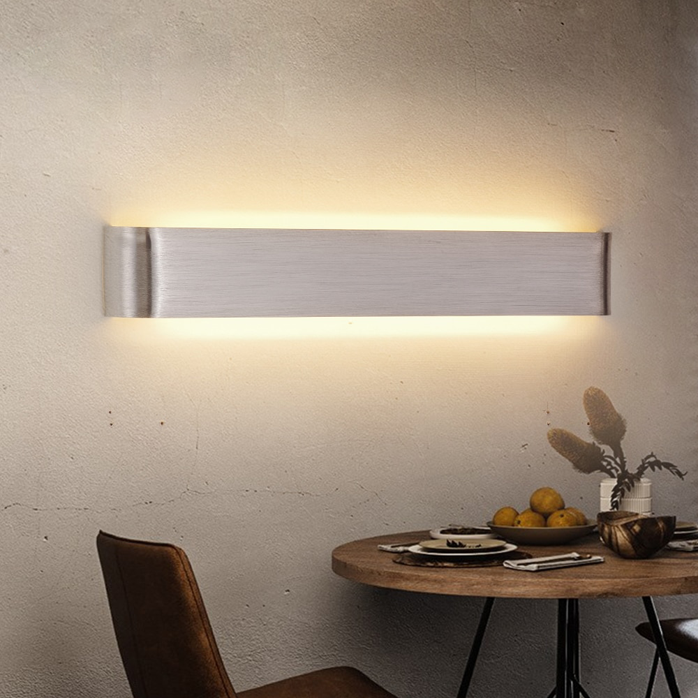 Silver linear wall sconce lit on a plaster wall above a table