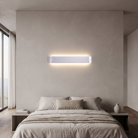 Silver linear LED wall sconce lit above a bed with pale bedding
