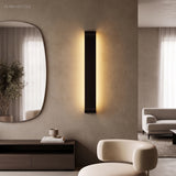 Black linear wall sconce mounted vertically beside a round mirror