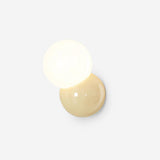 Studio view of the wall sconce with a butter yellow backplate and lit opal globe