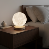 A glowing moon lamp sits on a dark wood bedside table next to a bed with white bedding and pillows.