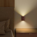 Dark wood sensor light lit on a wall beside a bed and lamp
