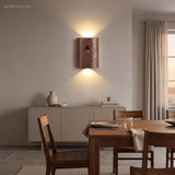Dark wood sensor wall light lit on a wall beside a dining table