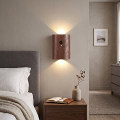 Dark wood motion sensor wall light lit beside a bed and nightstand