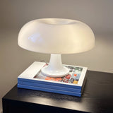 White mushroom table lamp lit on a stack of books on a dark surface