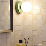 Green glass globe wall lamp on a tiled bathroom wall beside a mirror