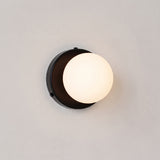 Frosted glass globe wall lamp with black backplate on a plain wall