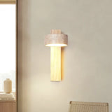 Natural wood wall sconce with upright travertine shade beside a woven chair