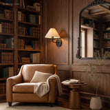 Fabric cone sconce on walnut bookshelves above a tan leather armchair
