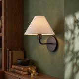 Black wall sconce with white tapered fabric shade on a green wall