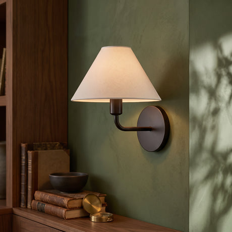 Black wall sconce with white tapered fabric shade on a green wall