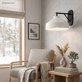 Black arm sconce with white shade beside a woven blind and armchair