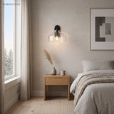 Clear glass sconce with black fitting above a bedroom nightstand