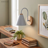 Grey cone shade sconce lit above a desk with books and a plant