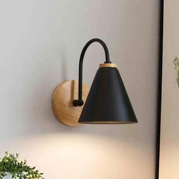 Black cone shade sconce on a wood mount lit on a white wall