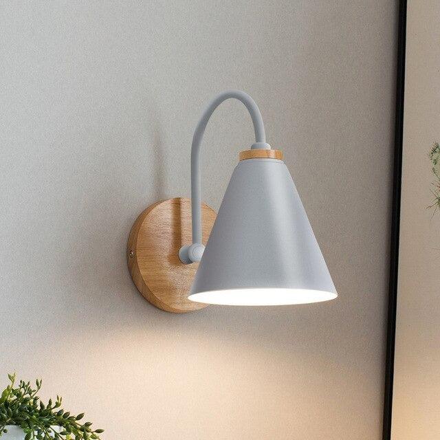 Grey cone shade sconce lit on a plain wall beside a plant