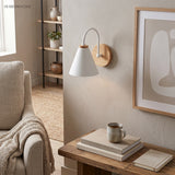White cone shade sconce on a wood mount lit above a side table