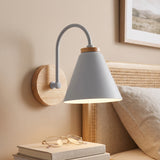Grey cone shade sconce on a wood mount lit above a bed