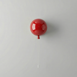 Small red balloon light on a plain wall with its pull cord