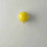 Yellow balloon light on a white wall with a long pull cord