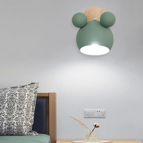 Green mouse wall light lit above a bed with a patterned cushion