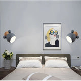 Two grey mouse wall lights lit either side of a bed with framed art
