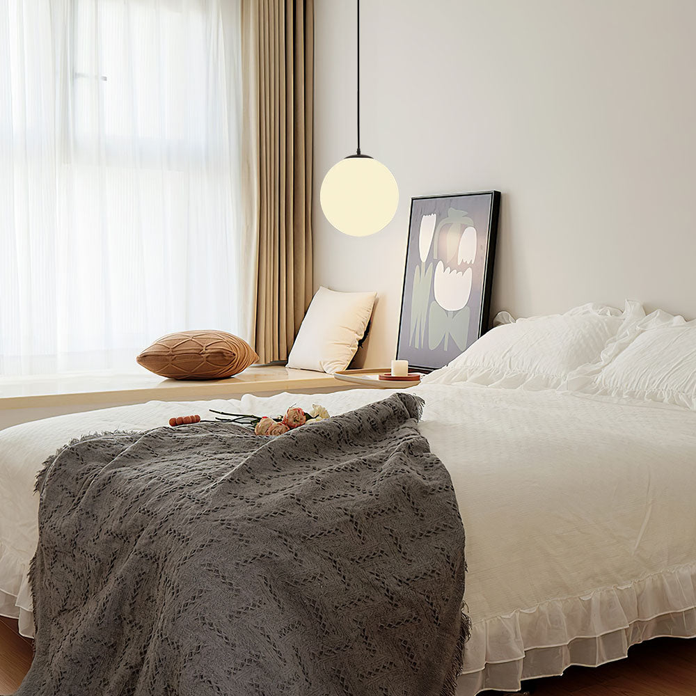 Single opal glass globe pendant hanging beside a bed on a black cord