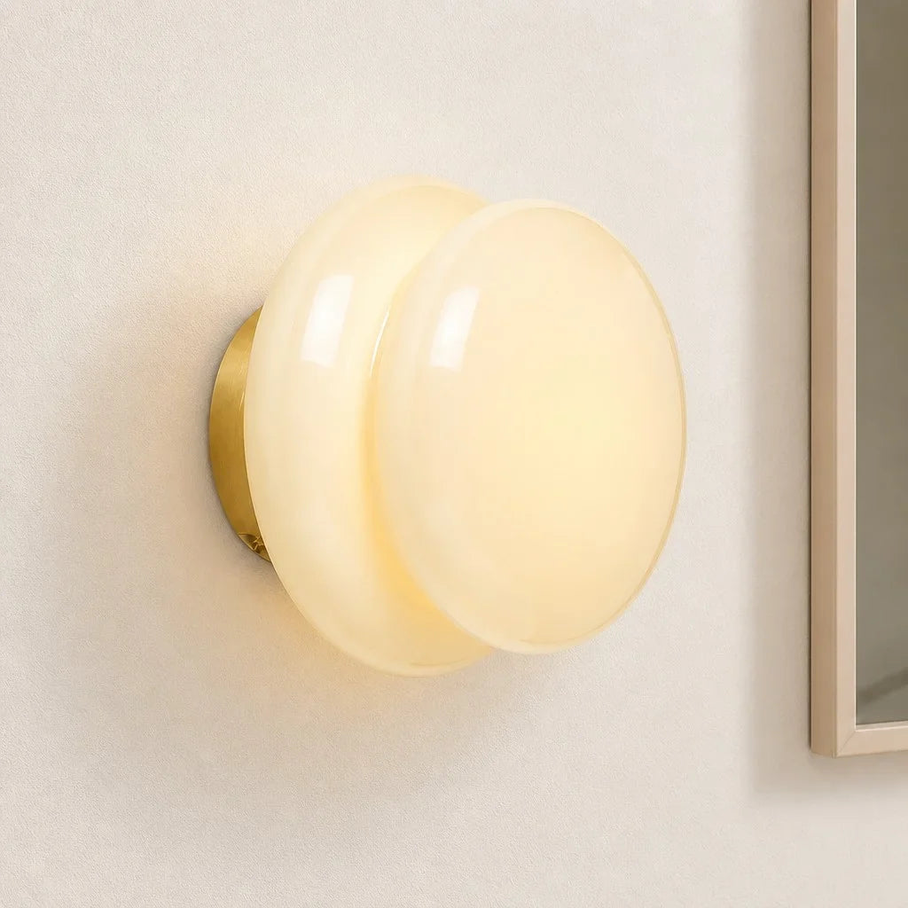 Pale cream glass wall sconce beside a framed mirror edge